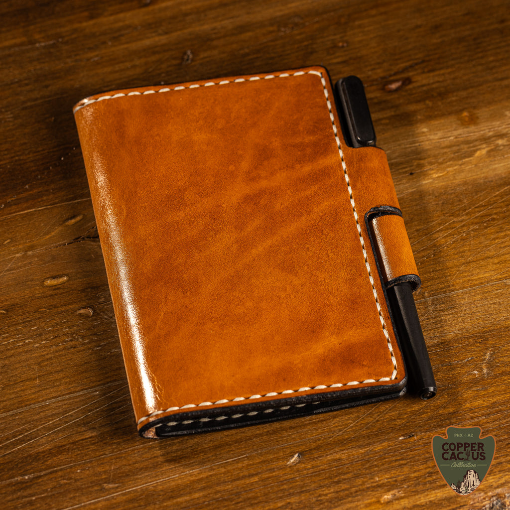 Brown leather notebook with pen holder on a wooden surface, featuring 'Copper Cactus' brand.